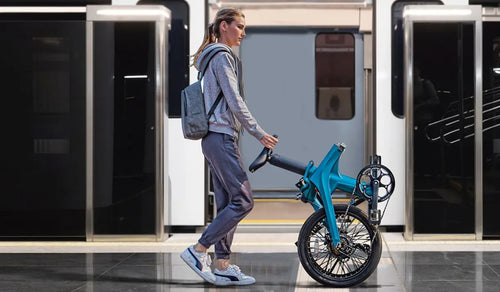 Una mujer caminando empujando una bicicleta eléctrica plegable.