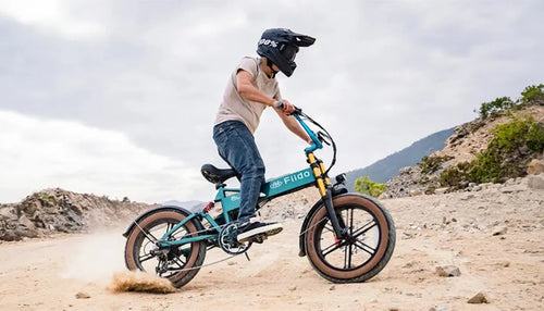 Un hombre montando una bicicleta eléctrica Fiido M1 Pro mejorada sobre la arena.