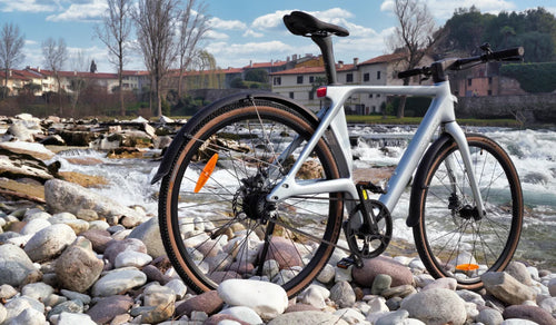Bicicleta eléctrica ultraligera de fibra de carbono Fiido Air expuesta en una orilla rocosa junto al agua corriente.