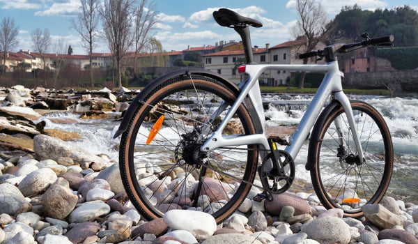 Bicicleta eléctrica ultraligera de fibra de carbono Fiido Air expuesta en una orilla rocosa junto al agua corriente.