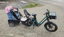 Se muestra una bicicleta eléctrica de carga Fiido T2 completamente cargada, con un asiento infantil, alforjas laterales, una caja de carga delantera y un remolque trasero muy cargado.