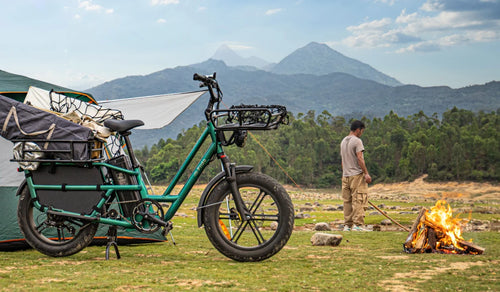Bicicleta eléctrica de carga Fiido T2 cargada con equipo de camping en un campamento de montaña, junto a una tienda de campaña y una fogata