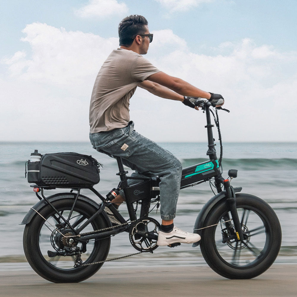 Vista lateral del hombre montando bicicleta eléctrica Fiido M1 Pro con bolsa en la playa