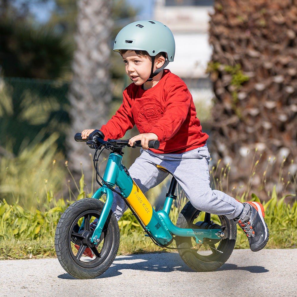 Un niño con casco monta en la bicicleta de equilibrio eléctrica Fiido Kidz